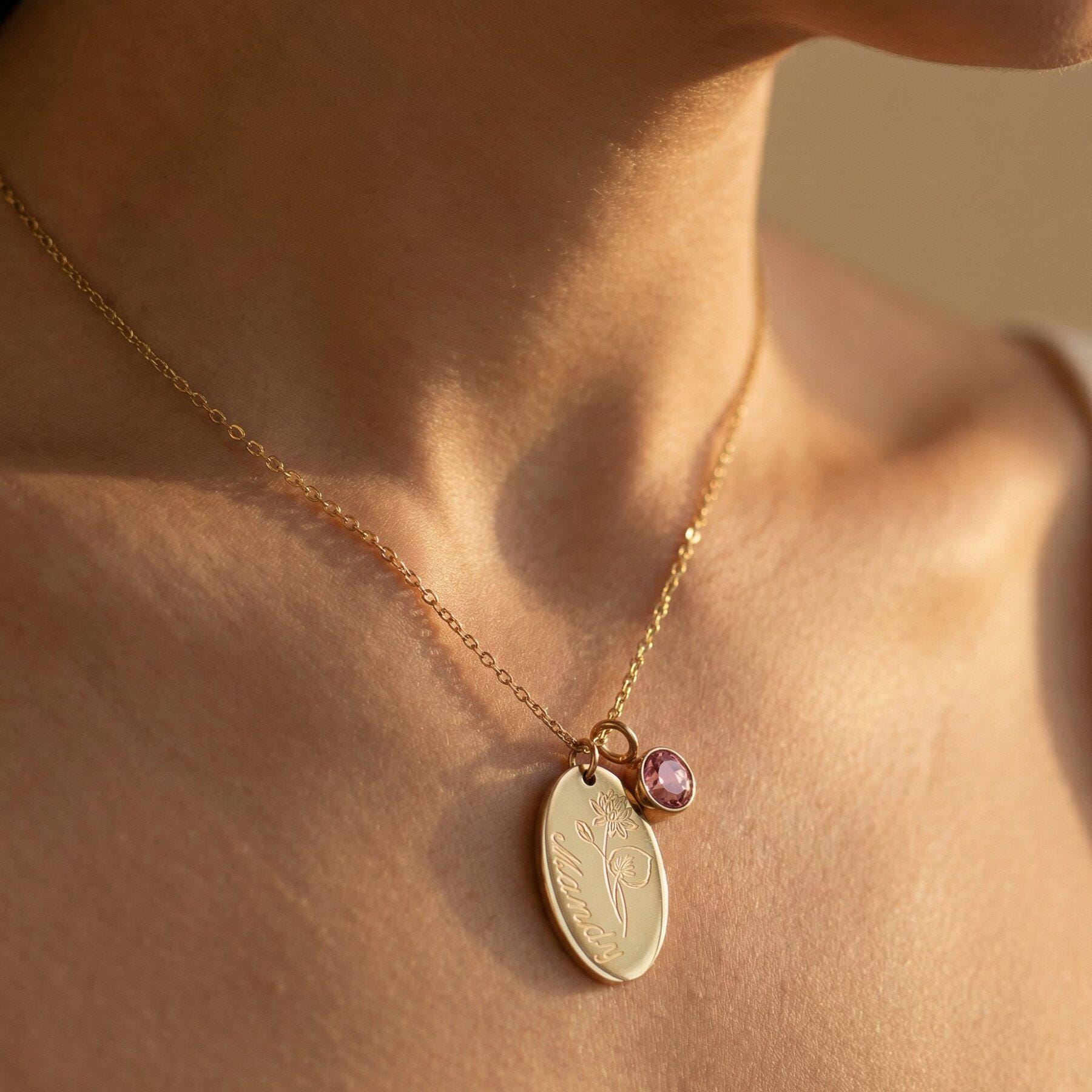 Frau trägt goldene Kette mit ovalem Gravur-Anhänger mit Geburtsblume und Name sowie rosa Geburtsstein-Charm – personalisierte Charms von Inaklam